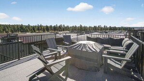 En tagterrasse med udendørs siddepladser, en overdækket bålplads og udsigt over et skovområde.