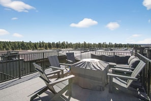 Une terrasse sur le toit avec des sièges extérieurs, un foyer extérieur abrité et une vue sur une zone boisée.