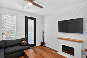 Un salon moderne avec une cheminée, un téléviseur à écran plat fixé au mur, un canapé foncé et une table basse en bois.