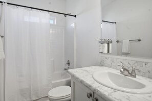 Een badkamer met douchegordijn, bad, toilet en wastafel met een marmeren blad, plus een spiegel.