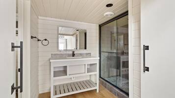 A bathroom with a white vanity, a glass shower enclosure, and a wooden floor.