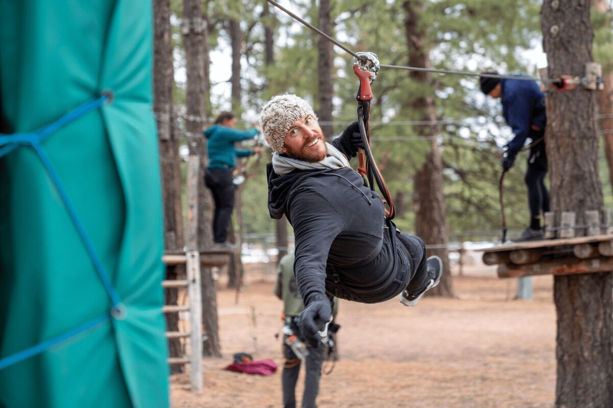 A person suspended on a zip line in a wooded area.