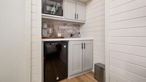 Cocina compacta con muebles blancos, lavavajillas, microondas y cubo de basura.