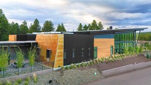 Un edificio moderno con una combinación de madera y paneles oscuros, rodeado de grava y pequeños árboles.