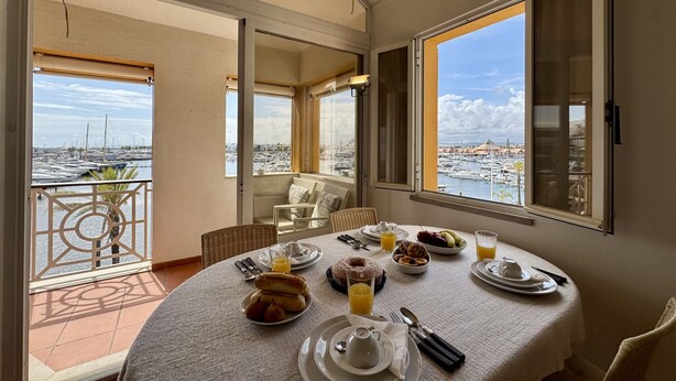 A balcony with a table set for breakfast, overlooking a marina with boats and buildings. - Vilamoura Marina Duplex 2 by Homing (Loulé)