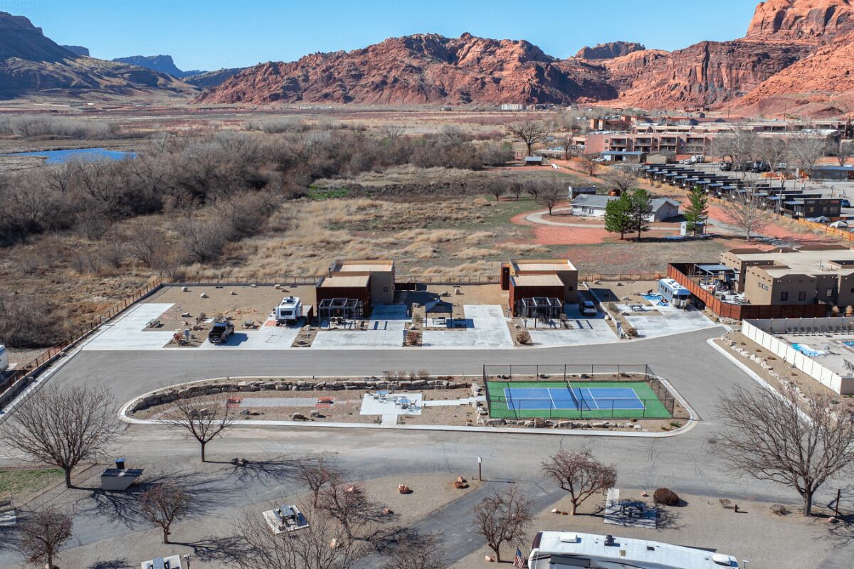 A hotel with a parking lot, tennis court, and a view of mountains.