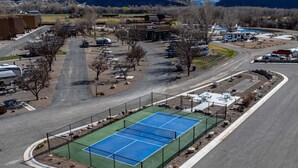 Ett flygbildsfoto av ett sportkomplex med en tennisbana, parkeringsområden och omgivande byggnader.