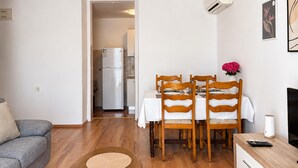 En kompakt opholdsstue med spiseplads, tekøkken og en grå sofa.