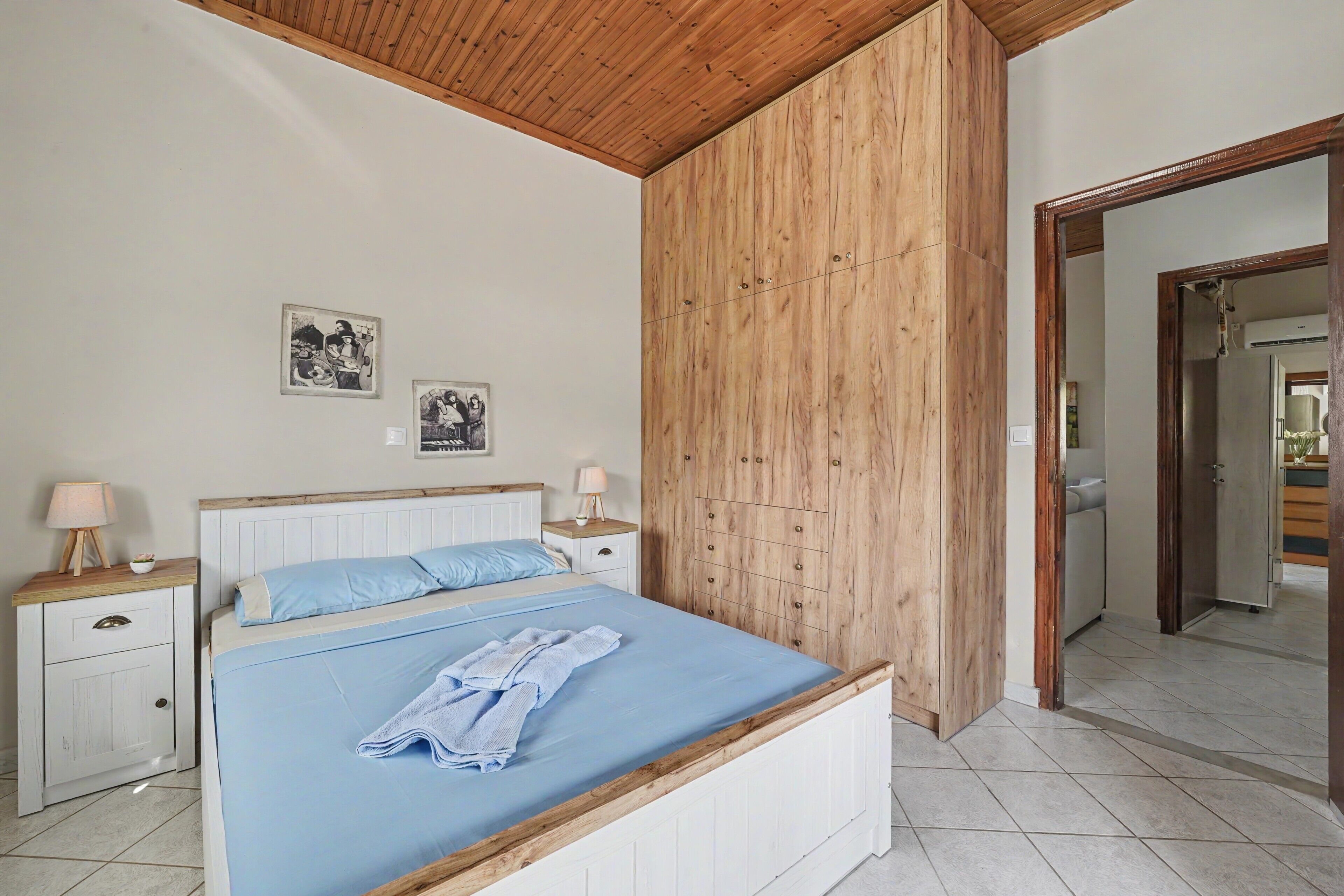 A bedroom with a wooden headboard, a bed with blue bedding, a nightstand with a lamp, and a wall-mounted picture.