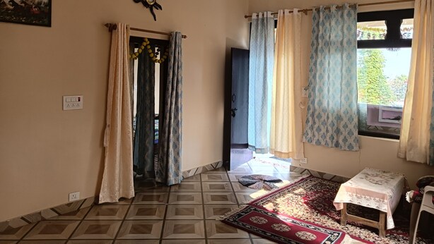 A room with a patterned rug, a small table, a door with curtains, and a wall clock. - We are not a commercial hotel... we are your home (Munsyari)