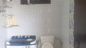 A compact bathroom with a washing machine, toilet, and a small window. - We are not a commercial hotel... we are your home (Munsyari)