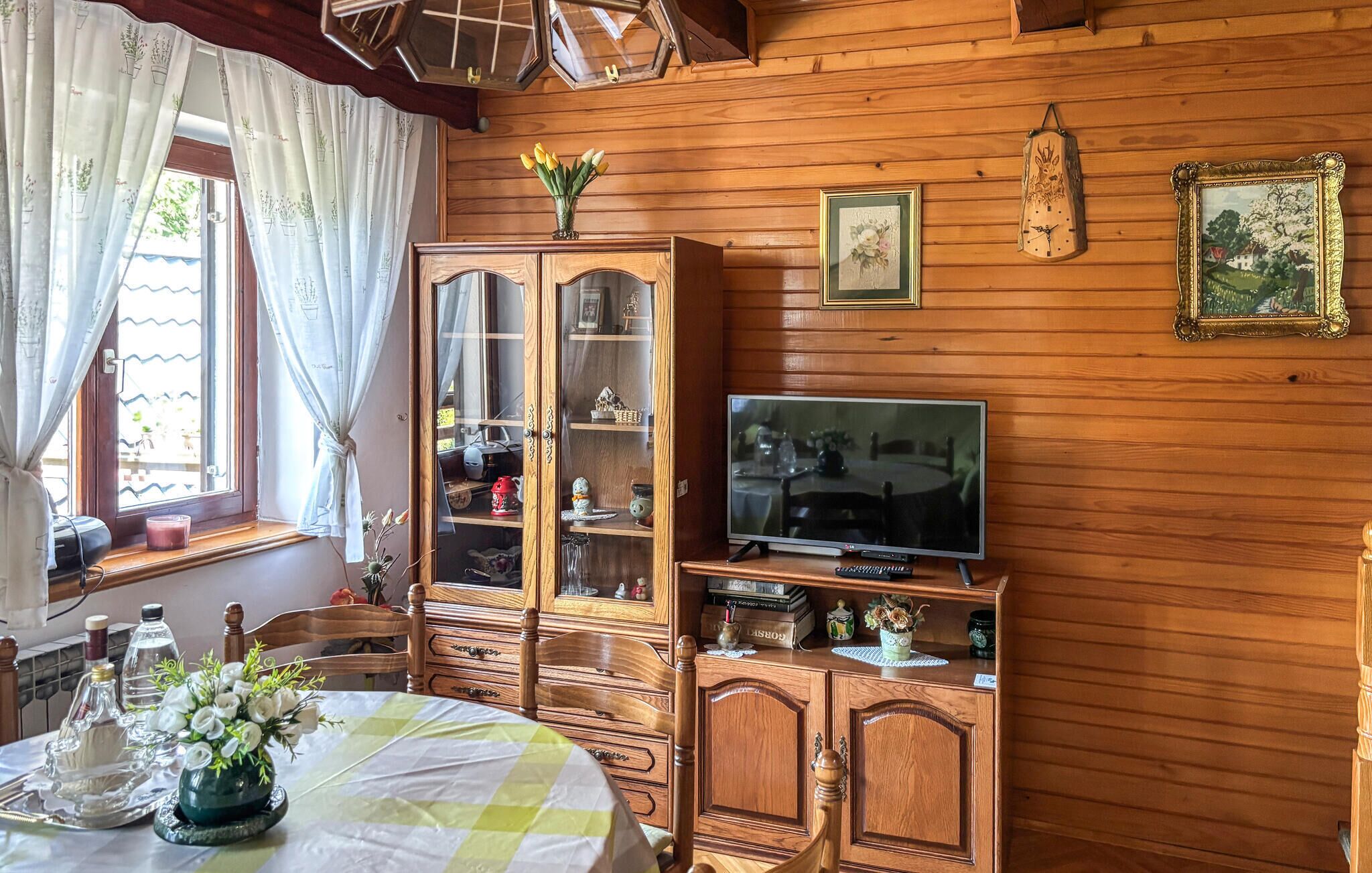 Una habitación con paneles de madera, un televisor, un aparador con puertas de vidrio y una mesa con mantel a cuadros.