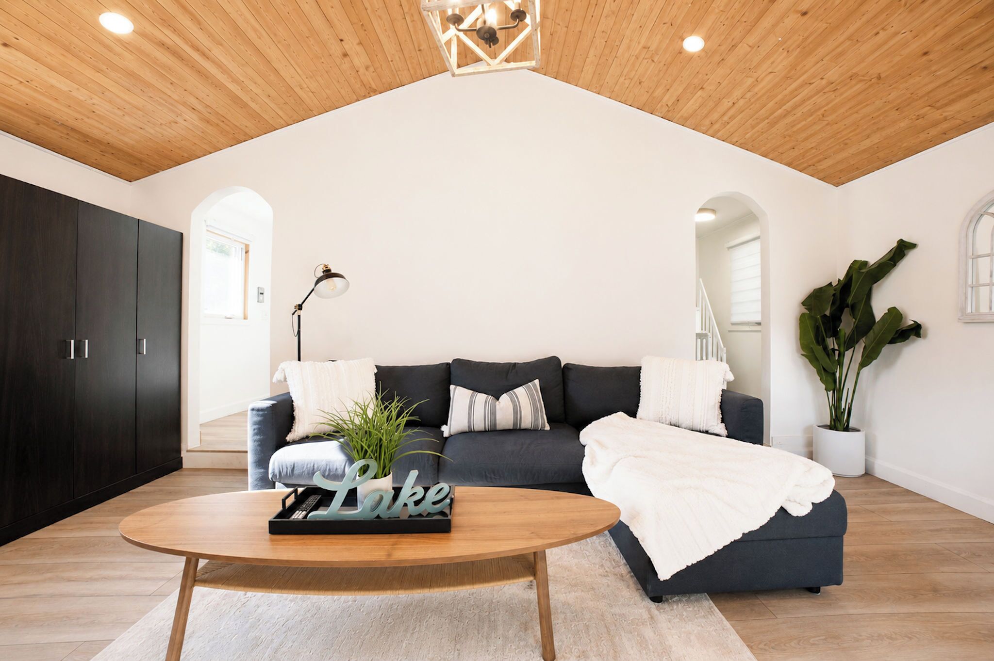 A modern living room with a high ceiling, dark-colored sofa, a round wooden coffee table, and a potted plant.