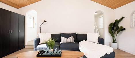 A modern living room with a high ceiling, dark-colored sofa, a round wooden coffee table, and a potted plant.