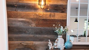 A room with a wooden wall, a blue chair, a white mug, a vase with flowers, and a blue lamp. - Bees Beach House: Luxury 5BR Sturgeon Lakefront w/ Private Sandy Beach & Sauna (Kawartha Lakes)
