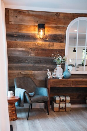 Ein Zimmer mit einer Holzwand, einem blauen Stuhl, einer weißen Tasse, einer Vase mit Blumen und einer blauen Lampe.