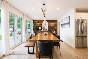 Eine moderne Küche mit einem Holztisch, schwarzen Stühlen, einem Edelstahlkühlschrank und einem großen Fenster mit Blick auf eine Terrasse.