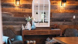A rustic interior with wooden walls, a large window, a wooden table, two chairs, a bench, and a wall-mounted light fixture. - Bees Beach House: Luxury 5BR Sturgeon Lakefront w/ Private Sandy Beach & Sauna (Kawartha Lakes)