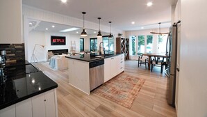 A modern kitchen with a central island, stainless steel appliances, pendant lighting, and a dining area with a view. - Bees Beach House: Luxury 5BR Sturgeon Lakefront w/ Private Sandy Beach & Sauna (Kawartha Lakes)