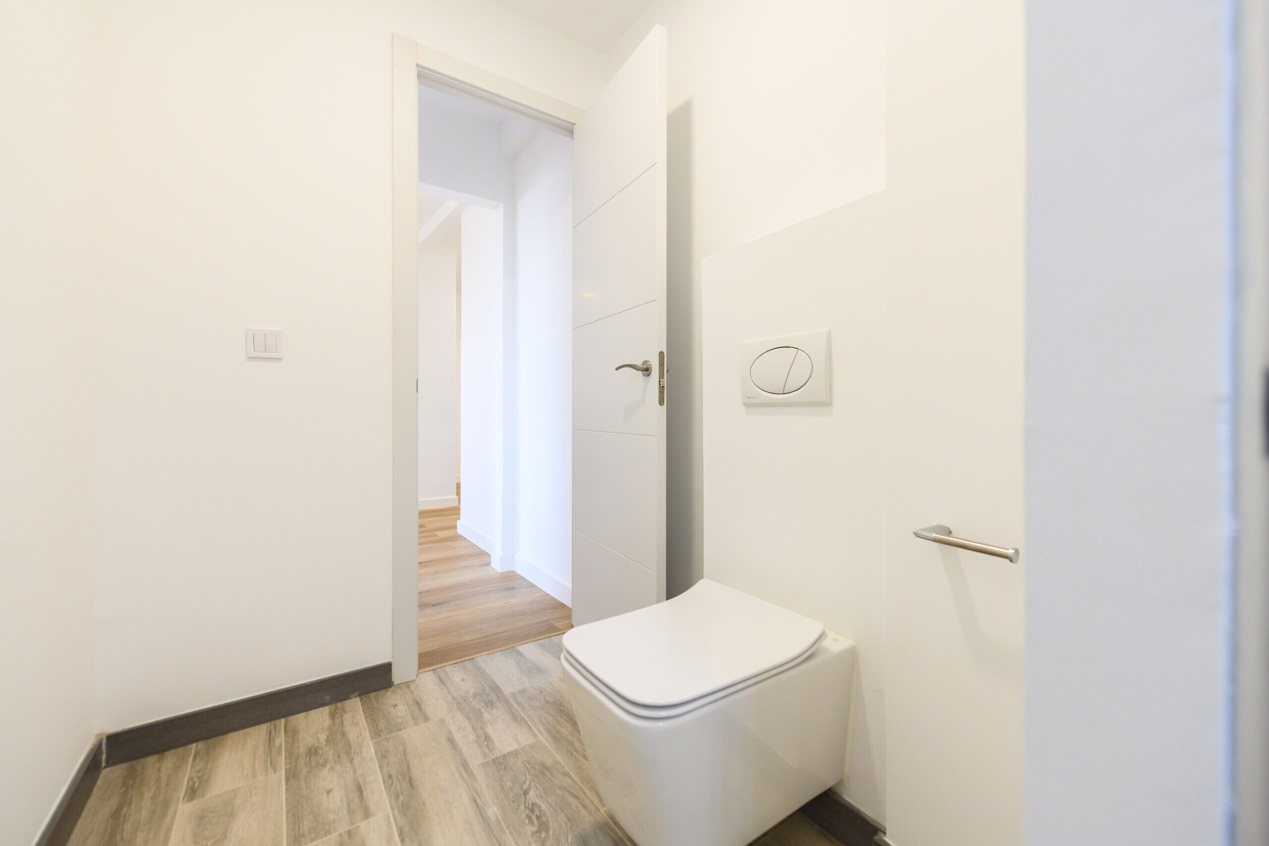 Ein schmaler Flur mit einer weißen Toilette, einem Holzboden und einer Tür zu einem anderen Raum.