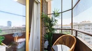 A balcony with a wicker chair, a potted plant, and a view of the cityscape. - 2-bedroom, 2-bathroom flat near the Bernabéu (Madrid)