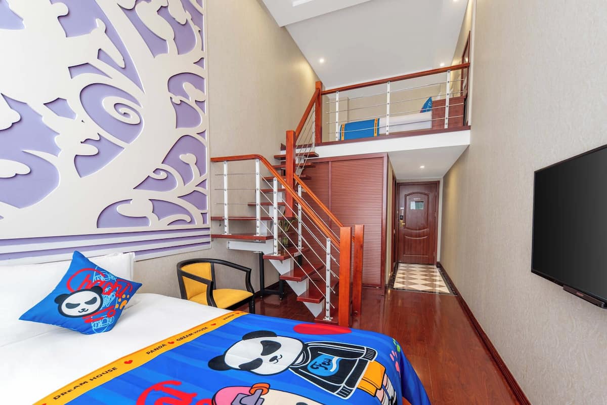 A hotel room with a bed, a chair, a TV, a staircase, and a decorative wall.