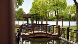 A wooden bridge over a body of water with a gazebo on the left and trees in the background. - Lu'an Garden Hotel Shanghai (Shanghai)