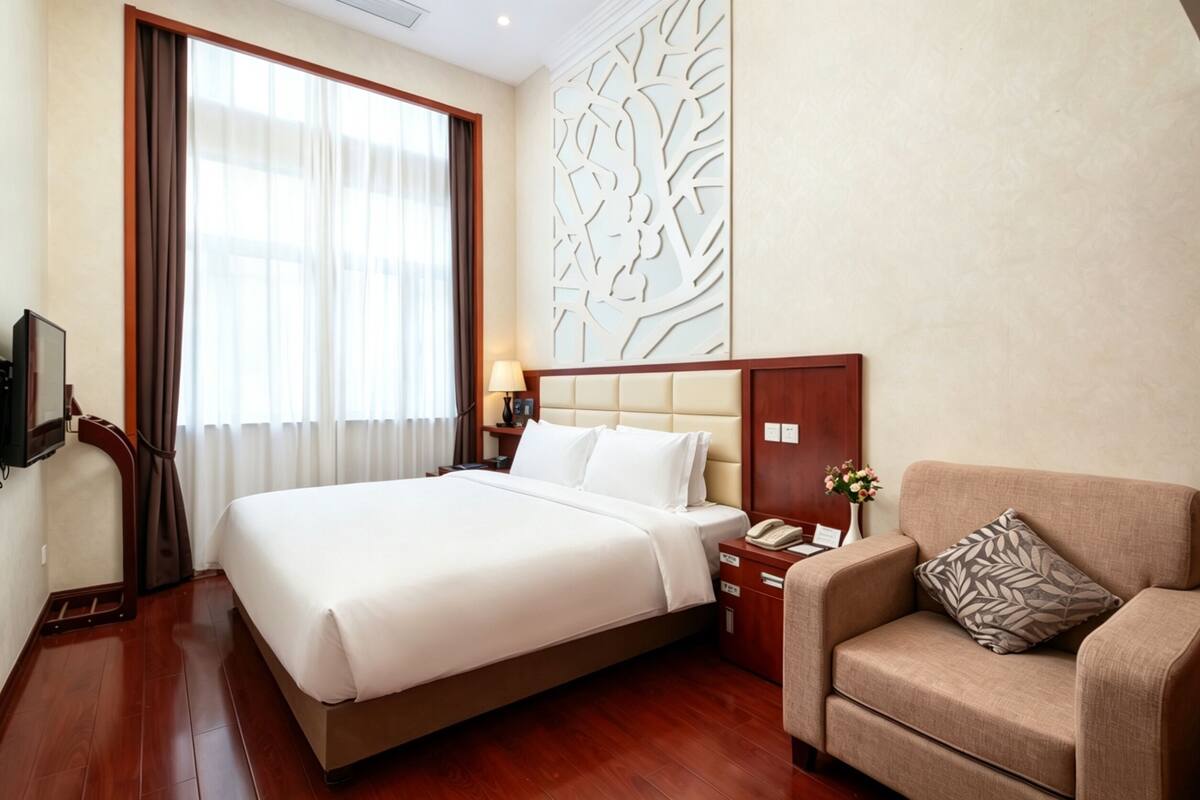 A hotel room with a large bed, a sofa, a wooden nightstand, a lamp, and a decorative wall panel.