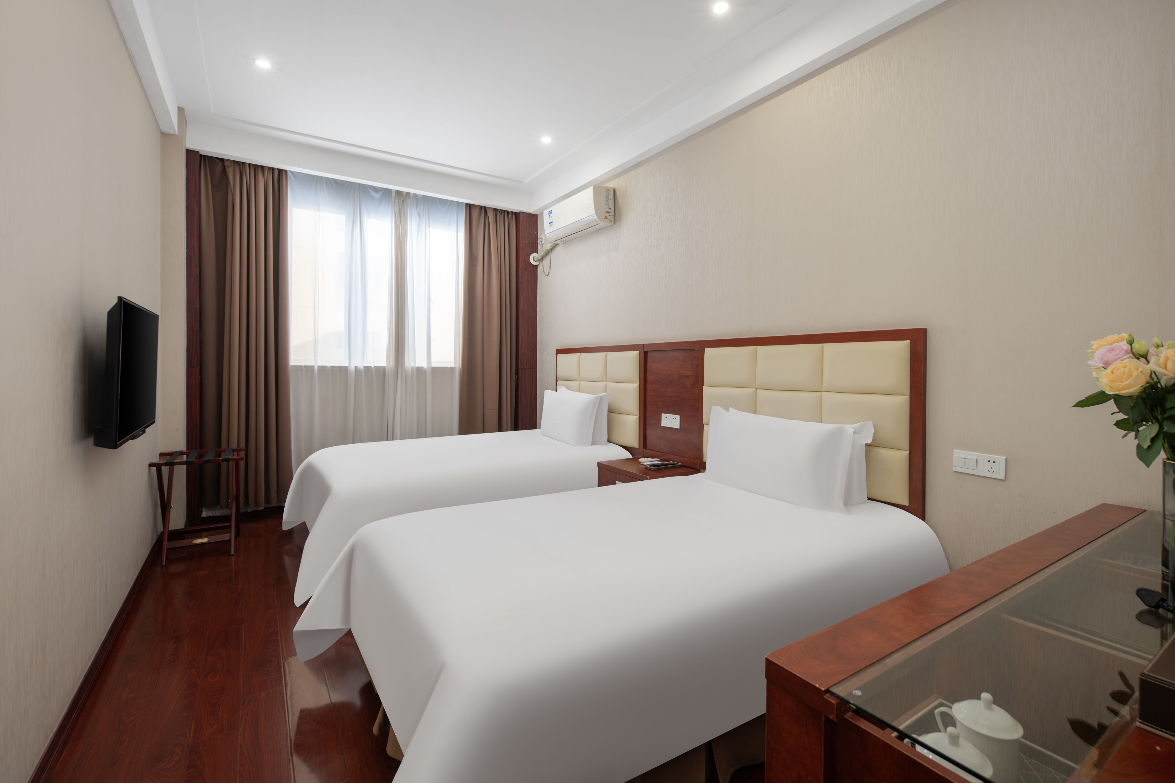 Habitación de hotel con dos camas, un televisor, un escritorio con superficie de vidrio y una ventana con cortinas.