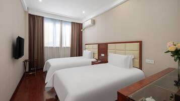 Habitación de hotel con dos camas, un televisor, un escritorio con superficie de vidrio y una ventana con cortinas.