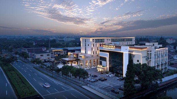 A modern hotel with a prominent entrance, multiple floors, and a parking lot. - Lu'an Garden Hotel Shanghai (Shanghai)