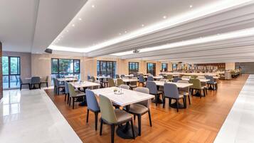 A spacious dining area with multiple tables and chairs, large windows, and a modern ceiling design.