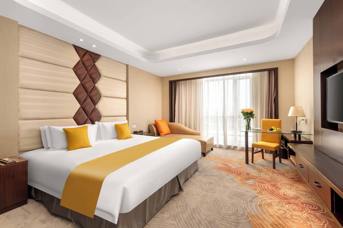 A hotel room with a large bed, a desk with a chair, a TV, and a window with curtains.