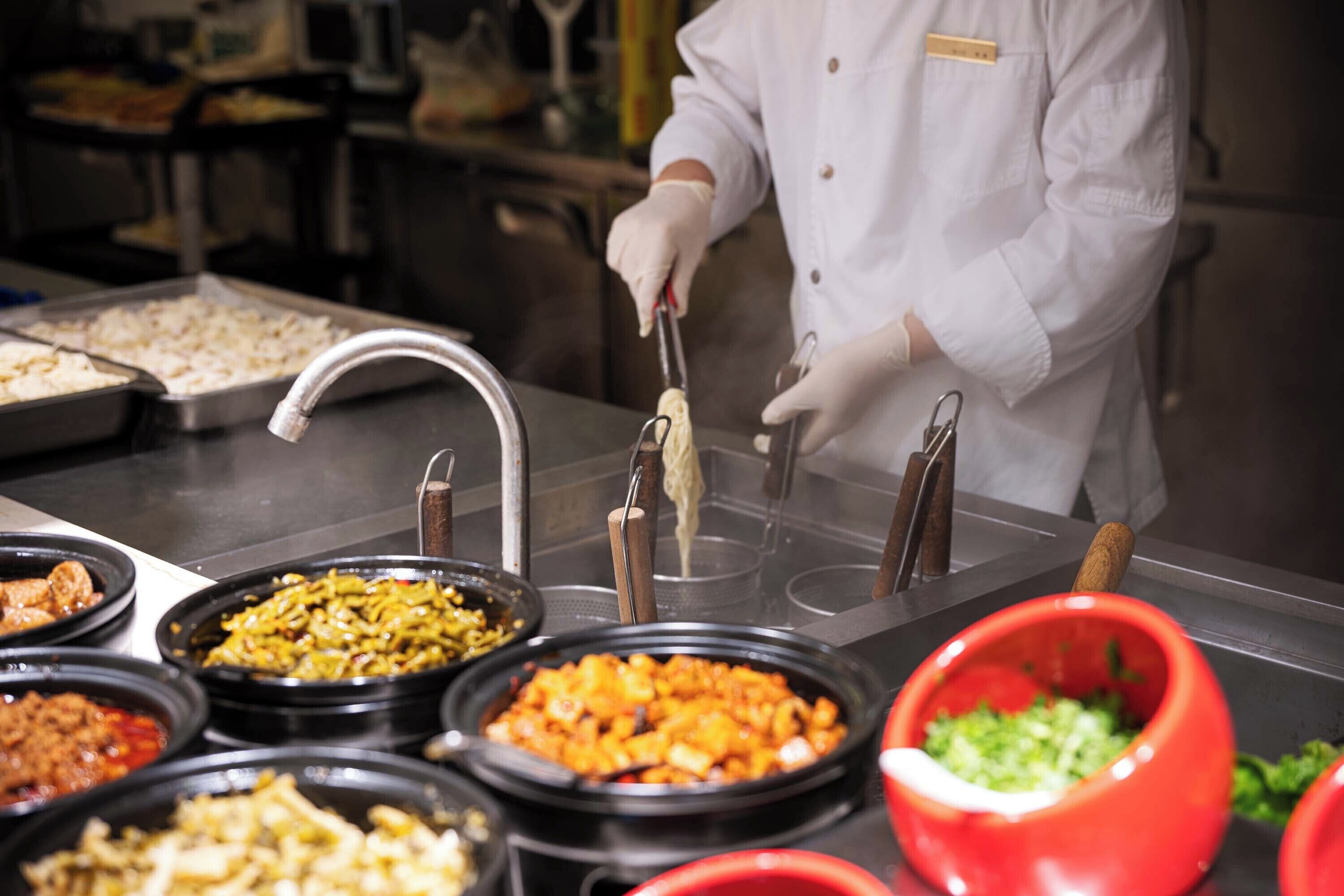 A person in a white coat preparing food in a kitchen with various dishes and utensils.