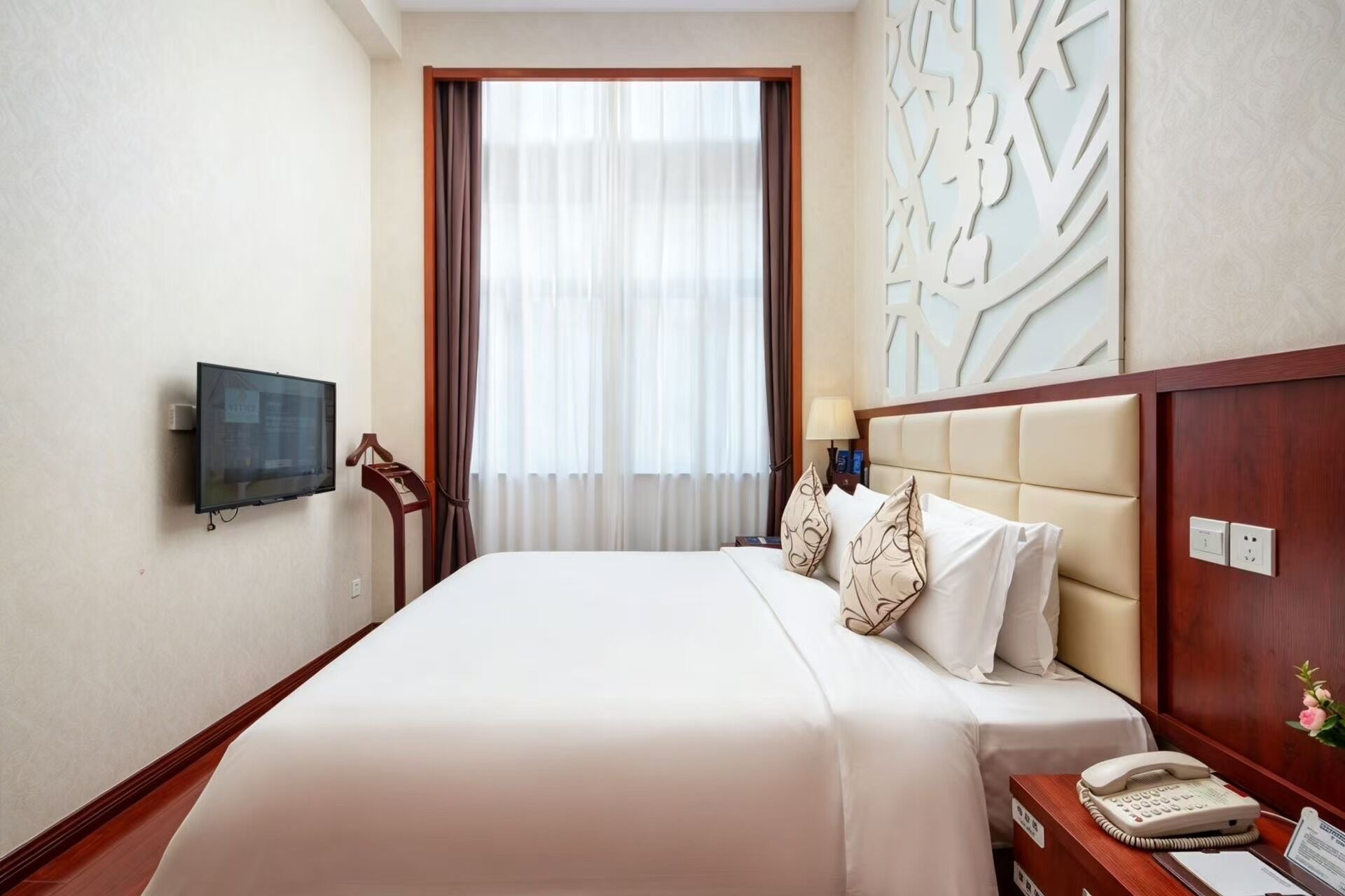A hotel room with a bed, a television, a telephone, and a decorative wall panel.