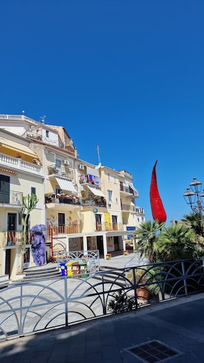 Rua com edifícios, uma bandeira vermelha e uma cerca de metal.