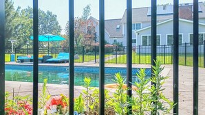 A swimming pool with a fence, a house in the background, and potted plants in the foreground. - Villa Sabrina (Lagrangeville)