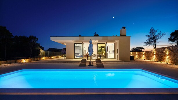Una casa moderna con piscina, area salotto esterna e un muro in pietra.