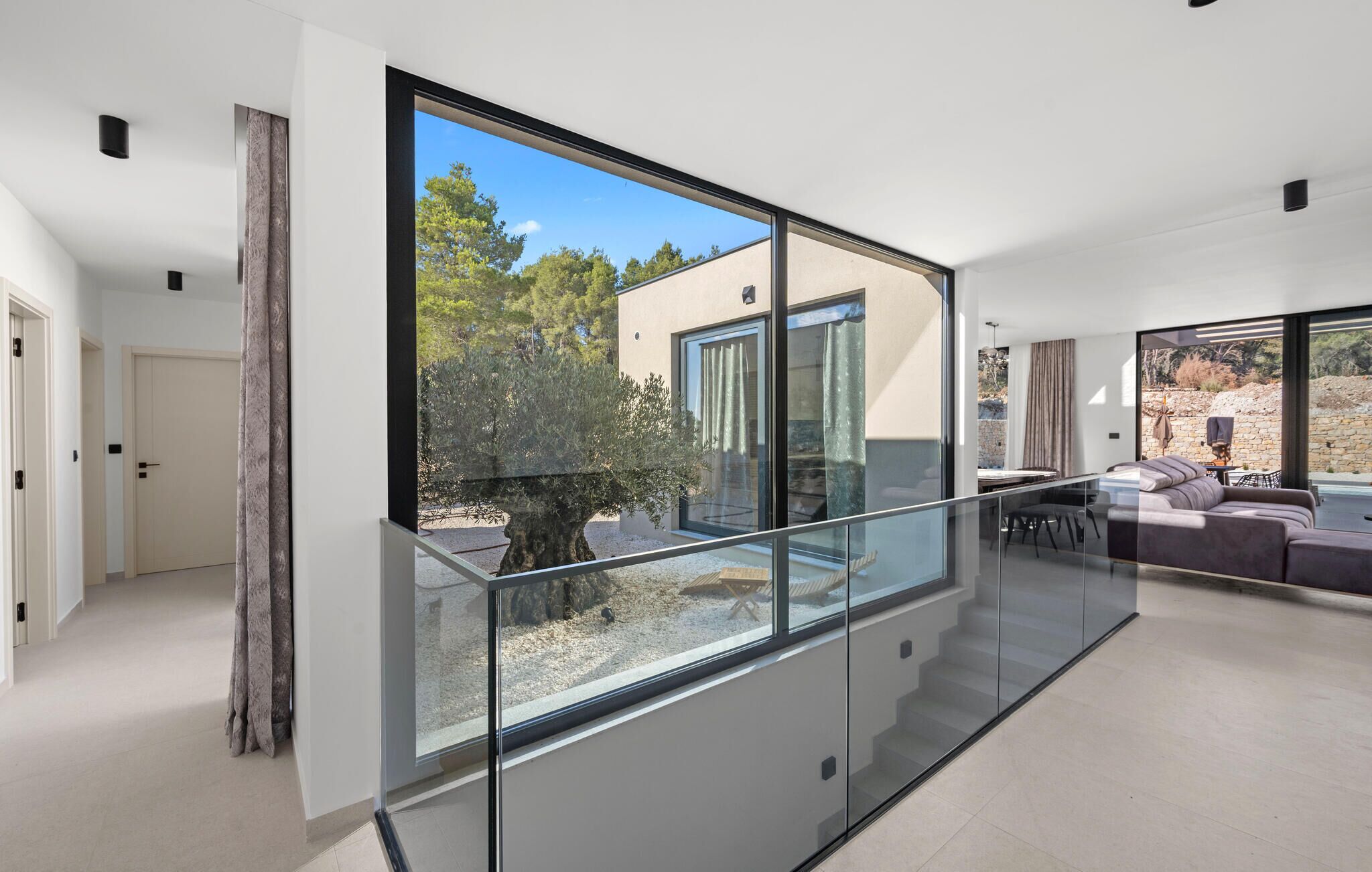 Un intérieur moderne avec un escalier en verre, un coin salon doté d’un canapé et une vue sur l’extérieur.