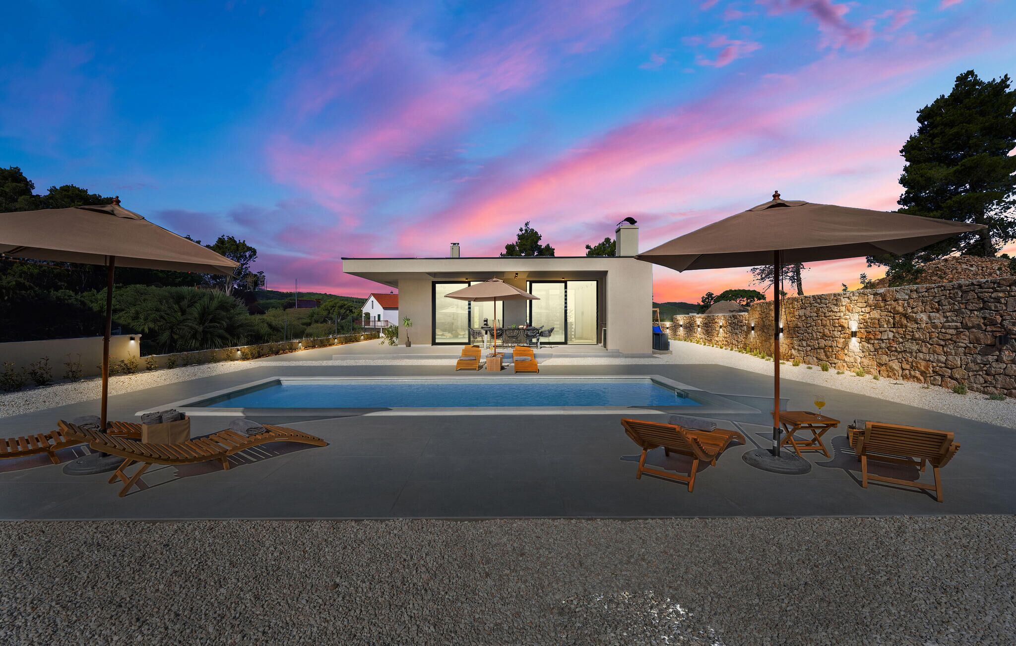 Una casa moderna con piscina, zona de estar exterior y un muro de piedra.