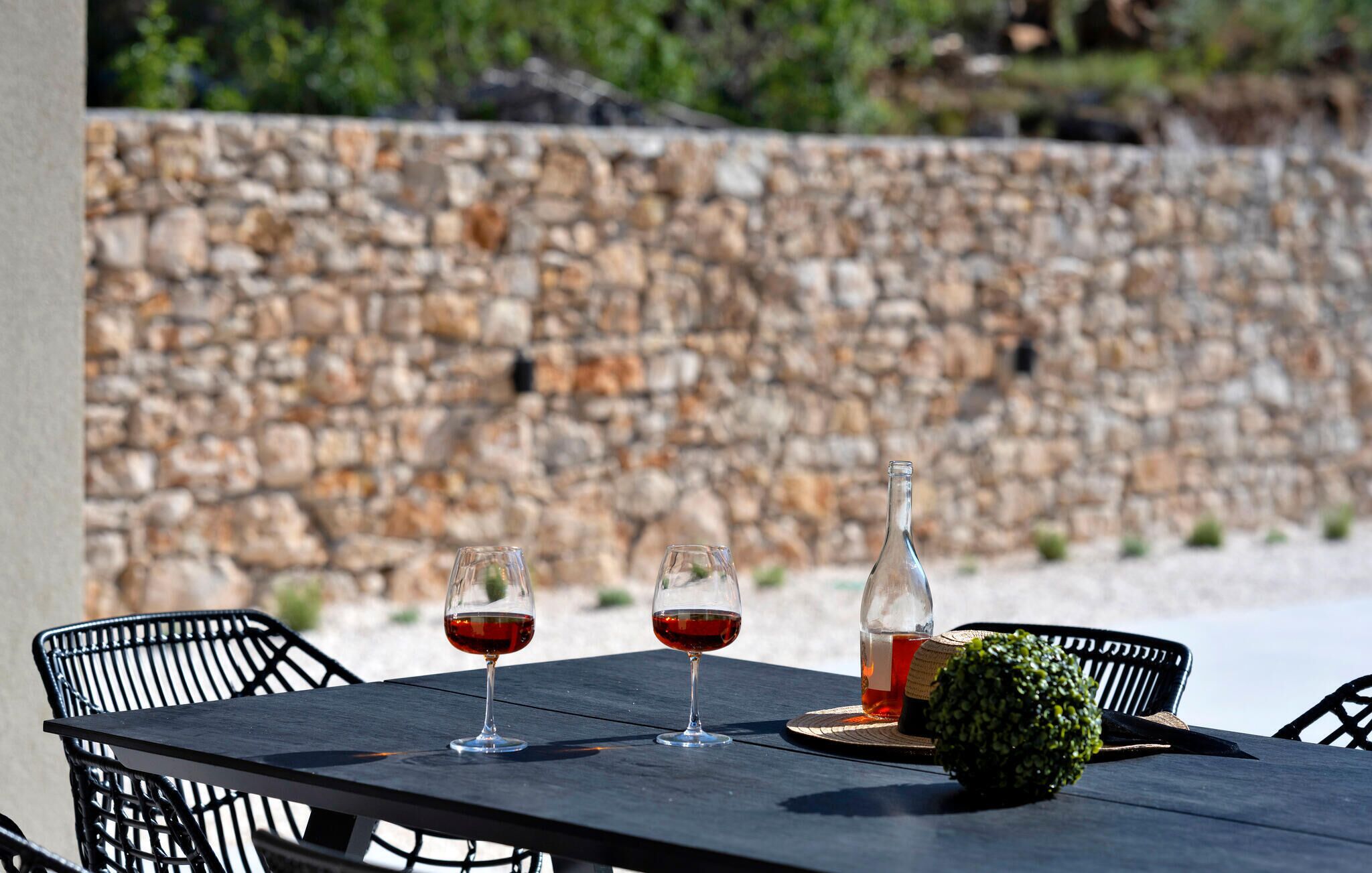 A table with two wine glasses and a bottle, set against a stone wall.