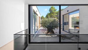 Un edificio moderno con un balcone in vetro, un albero e un vialetto ghiaioso.