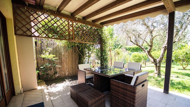 Un patio al aire libre con mobiliario de mimbre, una mesa con superficie de vidrio y una estructura de celosía.