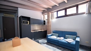 Cocina compacta con microondas, armarios y estufa. Hay un sofá azul con almohadas y una mesa con un bolso.