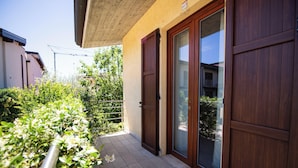 Un edificio residencial con una puerta de madera, un cerramiento de vidrio corredero y un patio con baldosas.