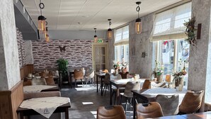 Interior de restaurante con paredes de piedra, mobiliario de madera e iluminación colgante. Las mesas están dispuestas con manteles y velas.