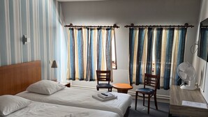 Habitación de hotel con dos camas, un escritorio, una silla, un ventilador de mesa y cortinas.