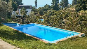 Ein rechteckiger Swimmingpool mit klarem, blauem Wasser, umgeben von Gras und Bäumen, mit Gebäuden im Hintergrund.