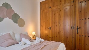 Ein Schlafzimmer mit Bett, Kissen, Decke, Nachttisch mit Lampe und einem Holzschrank.
