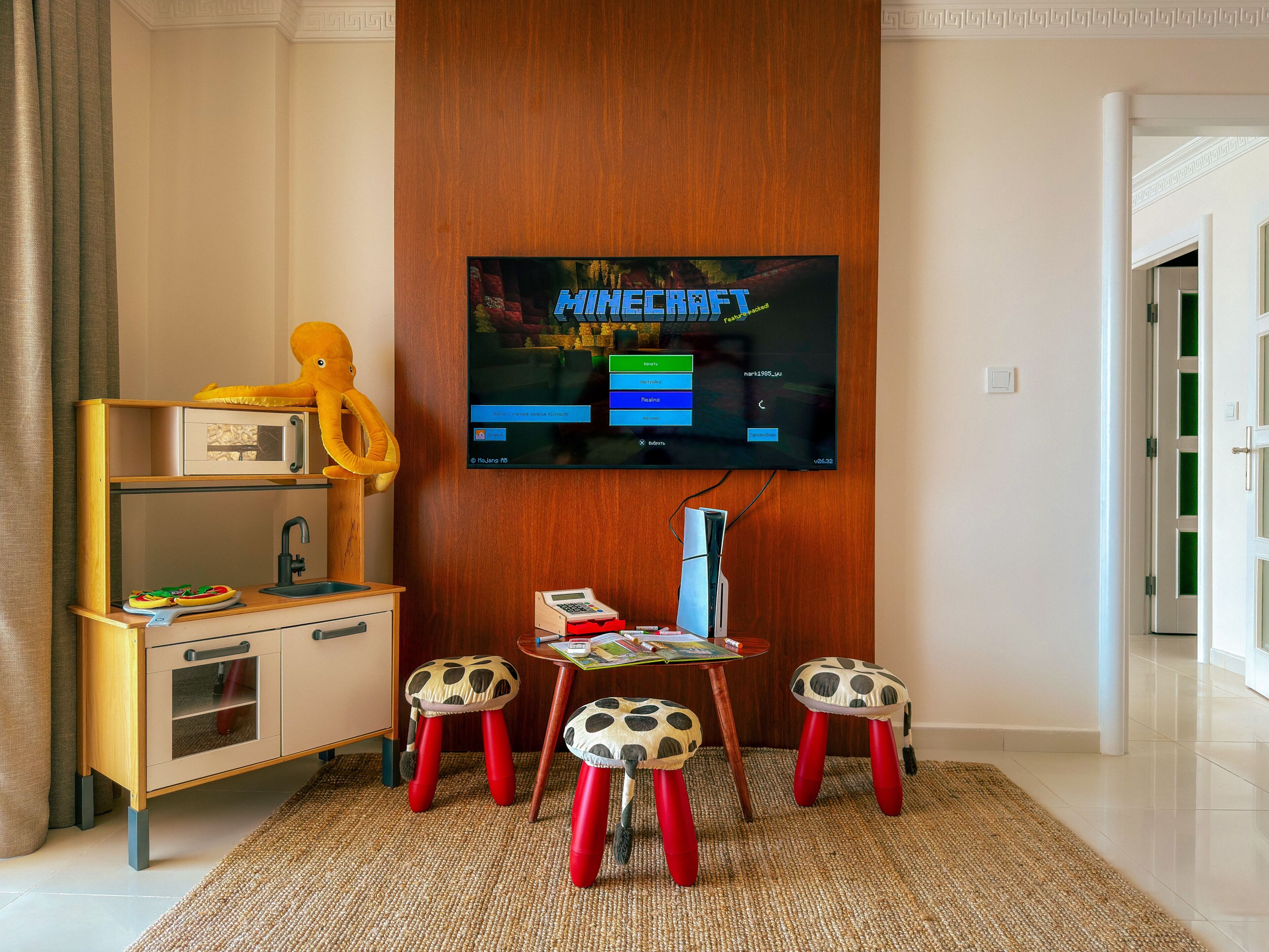 Een kamer met een televisie waarop een spel draait, een bureau met een stoel en een kleine tafel met krukken.